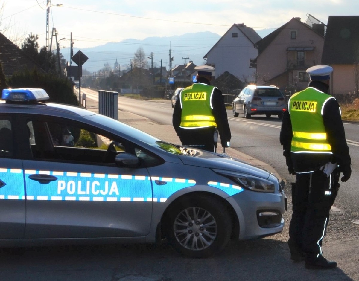 policjanci ruchu drogowego przy radiowozie, w tle jadący samochód