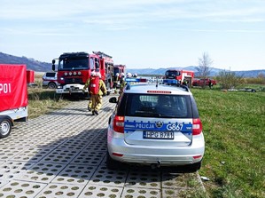 Ćwiczenia BESKID24 - Radiowóz policyjny, a w oddali strażacy i samochody strażackie