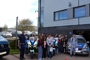 uczniowie i policjant ruchu drogowego, obok pojazdy służbowe