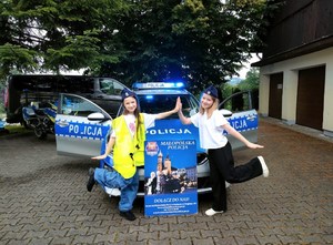 dwie dziewczynki przy radiowozie i plakacie zachęcającym do wstąpienia w szeregi Policji