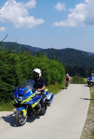 policjant na służbowym motocyklu, za nim kolarz