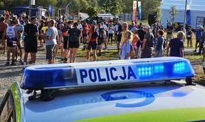 dach policyjnego radiowozu z lampą błyskową z napisem Policja, w tle uczestnicy Festiwalu Biegowego