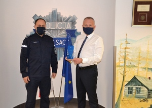 Komendant i prezydent L. Handzel na tle flag i policyjnej odznaki namalowanej na ścianie