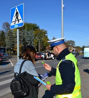 2. policjant drogówki wręcza pieszej elementy odblaskowe