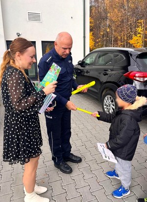 Policjant oraz przedstawicielka Urzędu Gminy Nawojowa rozdają dzieciom pamiątkowe odblaski i ulotki