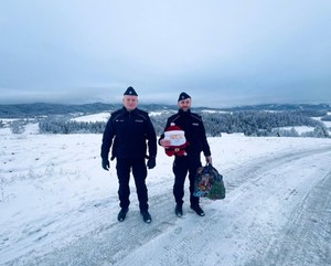 policjanci niosą upominki, w tle  zimowy krajobraz