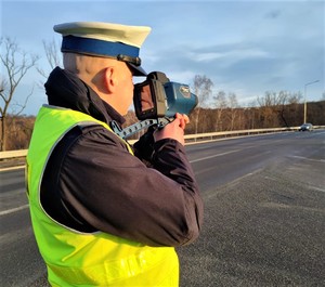 policjant ruchu drogowego z laserowym miernikiem prędkości, w oddali jadący samochód