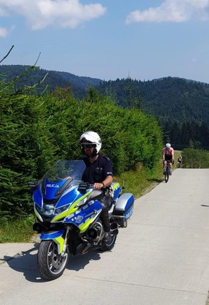 policjant na służbowym motocyklu, za nim kolarz