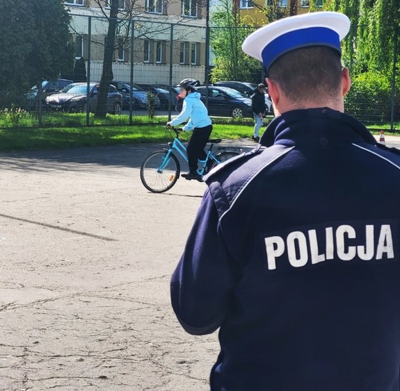 policjant ruchu drogowego odwrócony tyłem, w tle uczestnik turnieju jadący na rowerze - fot. archiwum KMP NS