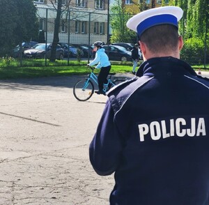policjant ruchu drogowego odwrócony tyłem, w tle uczestnik turnieju jadący na rowerze - fot. archiwum KMP NS