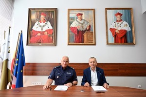 komendant i rektor siedzą przy stole, przed nimi dokumenty i pióra