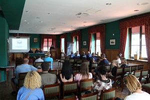 2. policjant prewencji przy mównicy, na krzesłach siedzą uczestnicy spotkania