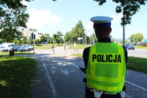 funkcjonariusz drogówki w kamizelce odblaskowej z napisem Policja, w tle uczestnicy ruchu drogowego w okolicy Ronda Solidarności