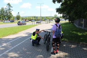 policjant drogówki sprawdza stan techniczny roweru, obok młody rowerzysta w kasku i z ochraniaczami na nogi