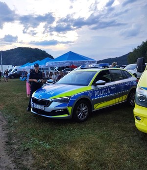 policjantka trzyma w ręku ulotki, obok radiowóz
