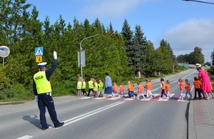 funkcjonariusz drogówki wstrzymuje ruch, uczniowie przechodzą przez przejście dla pieszych