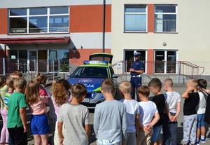 policjant drogówki przy radiowozie przed budyniem szkoły, obok uczniowie
