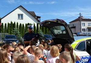 policjant przy radiowozie pokazuje dzieciom elementy umundurowania służbowego