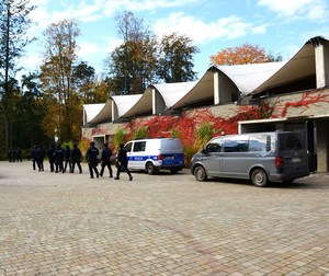 grupa policjantów przechodzi obok radiowozów zaparkowanych przy budynku