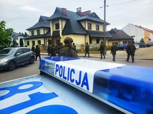 lampa z napisem Policja na dachu radiowozu, w tle strażnicy graniczni