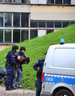 umundurowani policjanci prowadzą zatrzymanego do radiowozu