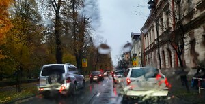 opady deszczu, samochody poruszają się ulicą, chodnikiem idą piesi z parasolami