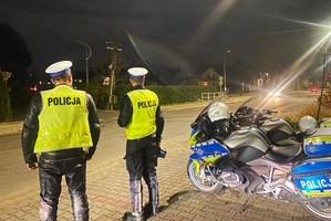 noc, policjanci ruchu drogowego obok policyjnego motocykla