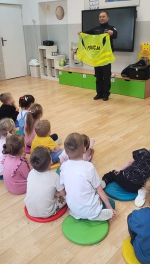 policjant pokazuje przedszkolakom kamizelkę odblaskową