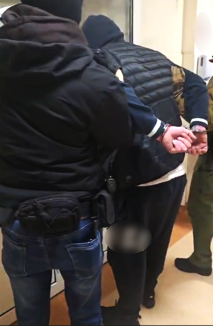 dwóch nieumundurowanych policjantów prowadzi zatrzymanego mężczyznę