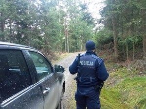 policjant na leśnej drodze, obok pojazd służbowy Straży Leśnej