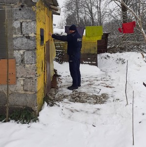 zima, policjant puka do drzwi małego budynku z pustaków