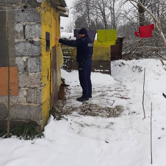 zima, policjant puka do drzwi małego budynku z pustaków