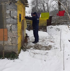 zima, policjant puka do drzwi małego budynku z pustaków