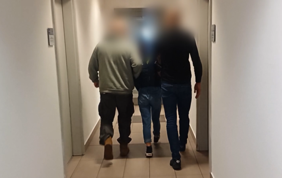 nieumundurowani policjanci prowadzą zatrzymaną kobietę