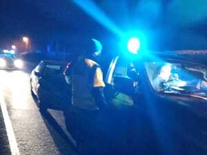 noc, błyska lampa radiowozu (tzw. kogut) - policjant stoi przy nieoznakowanym radiowozie i zatrzymanym pojeździe, w tle oznakowany radiowóz