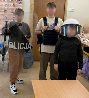 trzech chłopców w policyjnym kasku, kamizelce i z tarczą ochronną