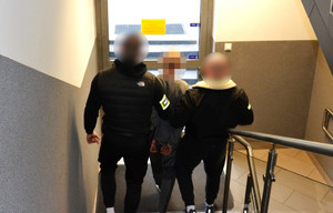 nieumundurowani policjanci prowadzą zatrzymanego po schodach w kierunku wyjścia z budynku