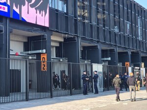 kilku umundurowanych policjantów przy ogrodzeniu stadionu, obok przechodzą kibice