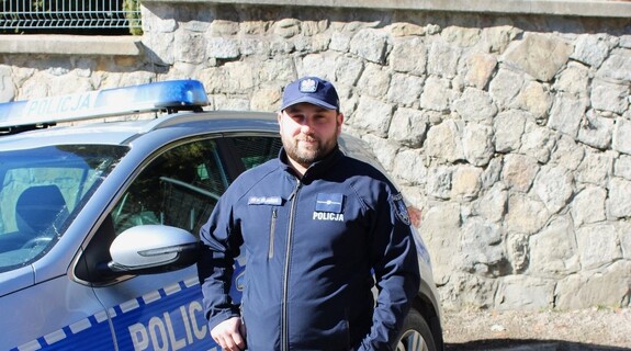 Piotr Kiliański w policyjnym mundurze przy radiowozie