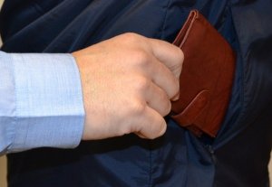męska dłoń wyciąga portfel schowany w kieszeni kurtki innego mężczyzny