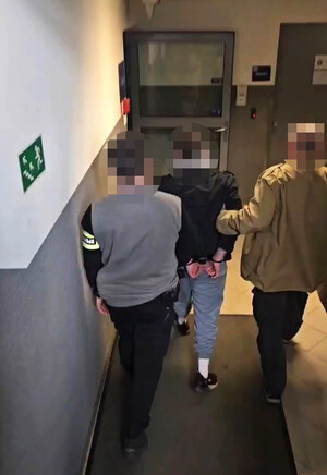 nieumundurowani policjanci prowadzą zatrzymanego korytarzem