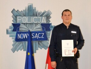 asp. sztab. Paweł Poręba z legitymacją i listem gratulacyjnym  przy logo sądeckiej komendy
