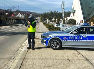 policjant ruchu drogowego z laserowym miernikiem prędkości, obok oznakowany radiowóz - fot. archiwalne