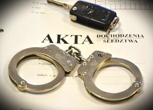 kajdanki oraz kluczyk do samochodu położone na okładce akt