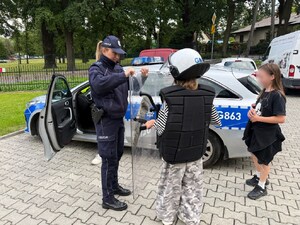 dziecko w elementach ochronnych umundurowania policyjnego, obok dziewczynka i policjantka