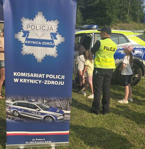Dzieci oglądają  oznakowany radiowóz. Obok umundurowany policjant.