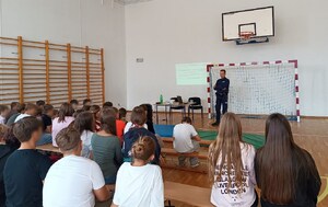 policjant i uczniowie podczas prelekcji zorganizowanej w sali gimnastycznej szkoły