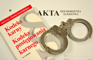 okładka akt, na niej kodeks karny i postępowania karnego, obok kajdanki