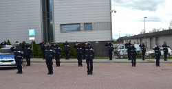 radiowóz oznakowany, grupa kilkunastu policjantów salutuje przed budynkiem komendy