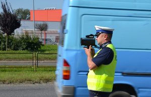 policjant ruchu drogowego z laserowym miernikiem prędkości, w tle przejeżdżający bus